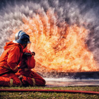 Firefighter in fire fighting suit spraying water, Firemen fighting  raging fire with huge flames of burning, Fire prevention and extinguishing concept