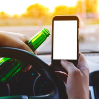 Man drinking behind the wheel holding a phone