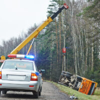 Police with flasher signal while crane pulls truck from accident site