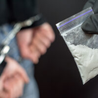 Police arrest drug trafficker with handcuffs. police officer finds A Little Bag Of Drugs during the search of drug dealer