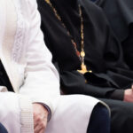 A Muslim mullah in white clothes and a Christian priest in a black cassock are sitting next to each other. The concept of religious cooperation, understanding, tolerance and friendship. A Muslim mullah in white clothes and a Christian priest in a black cassock are sitting next to each other. The concept of religious cooperation, understanding, tolerance and friendship.