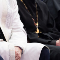 A Muslim mullah in white clothes and a Christian priest in a black cassock are sitting next to each other. The concept of religious cooperation, understanding, tolerance and friendship.