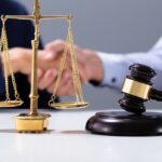 Gavel And Golden Justice Scale In Front Of Shaking Hands Gavel And Golden Justice Scale In Front Of Shaking Hands