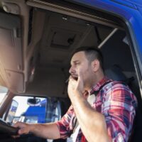 Truck driver yawning while driving. Trucker feeling sleepy and tired after long ride. Overworked people at job.