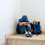 Sad boy with backpack sitting alone in the corner in the staircase Sad boy with backpack sitting alone in the corner in the staircase