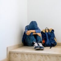 Sad boy with backpack sitting alone in the corner in the staircase