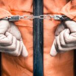 Handcuffed hands of a prisoner behind the bars of a prison Handcuffed hands of a prisoner behind the bars of a prison
