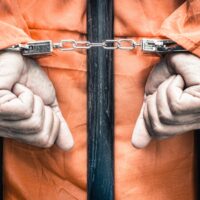 Handcuffed hands of a prisoner behind the bars of a prison Handcuffed hands of a prisoner behind the bars of a prison