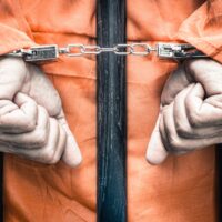 Handcuffed hands of a prisoner behind the bars of a prison