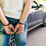 an offender standing in handcuffs near the car. Concept of arrest the driver, violation of rules and drinking alcohol while driving the car an offender standing in handcuffs near the car. Concept of arrest the driver, violation of rules and drinking alcohol while driving the car