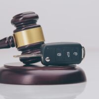 Close-up Of Gavel And Car Key On Sounding Block Against Grey Close-up Of Gavel And Car Key On Sounding Block Against Grey