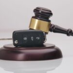 Close-up Of Gavel And Car Key On Sounding Block Against Grey Close-up Of Gavel And Car Key On Sounding Block Against Grey