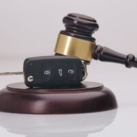 Close-up Of Gavel And Car Key On Sounding Block Against Grey Close-up Of Gavel And Car Key On Sounding Block Against Grey