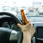A driver holding alcoholic bottle while driving / Drunk driving concept A driver holding alcoholic bottle while driving / Drunk driving concept