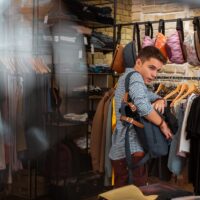 Hiding clothes. Quick professional thief hiding new clothes into his big backpack while stealing in a fashionable shop