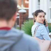 Young Woman Calling For Help On Mobile Phone Whilst Being Stalked On City Street By Man