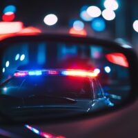 View from the passenger seat rearview mirror showing a vehicle being pulled over by a police car, capturing a moment of a traffic stop, law enforcement intervention, and road safety precautions