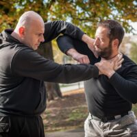 Two men are practicing self-defense techniques outdoors in a park.