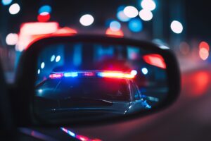 View from the passenger seat rearview mirror showing a vehicle being pulled over by a police car, capturing a moment of a traffic stop, law enforcement intervention, and road safety precautions