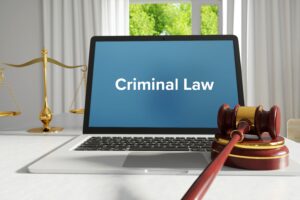 Laptop showing "Criminal Law" on screen sits on table with a gavel in front and balance scales behind, suggesting a legal and authoritative tone.