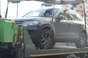 A gray SUV is secured on a flatbed tow truck in an urban setting. The vehicle is strapped down, indicating it