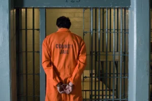 Handcuffed male criminal wearing prison uniform stands in jail