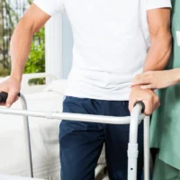 Nurse Assisting Senior Man With Walker In Rehab Center