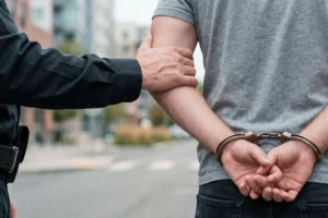 Downloaded File #: 2167682756 Police officer holding the arm of a handcuffed man during an arrest on a city street, escorting the suspect. Concept of law enforcement, crime detention, criminal justice